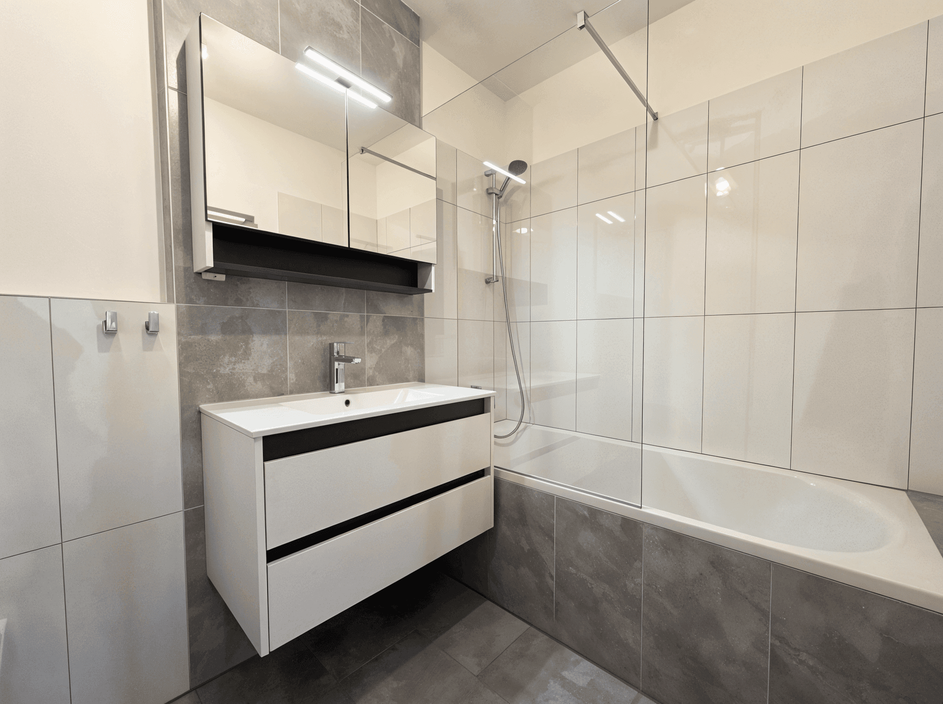 Modernes Badezimmer mit Badewanne, Dusche und eleganten grauen Fliesen.