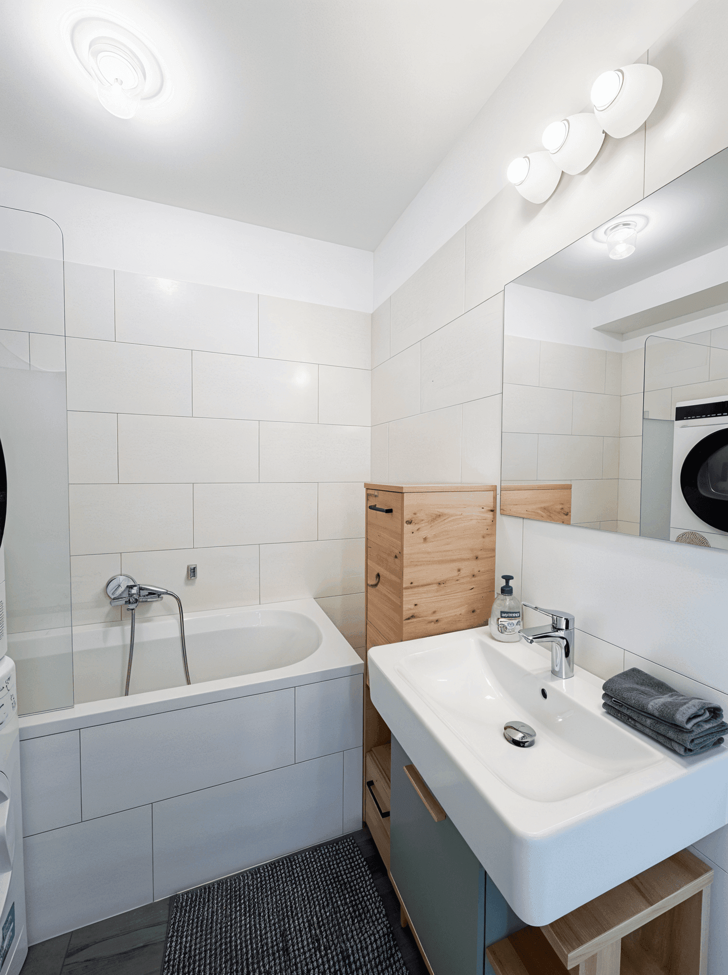Modernes Badezimmer mit Badewanne, Waschbecken und Waschmaschine in hellen Fliesen.