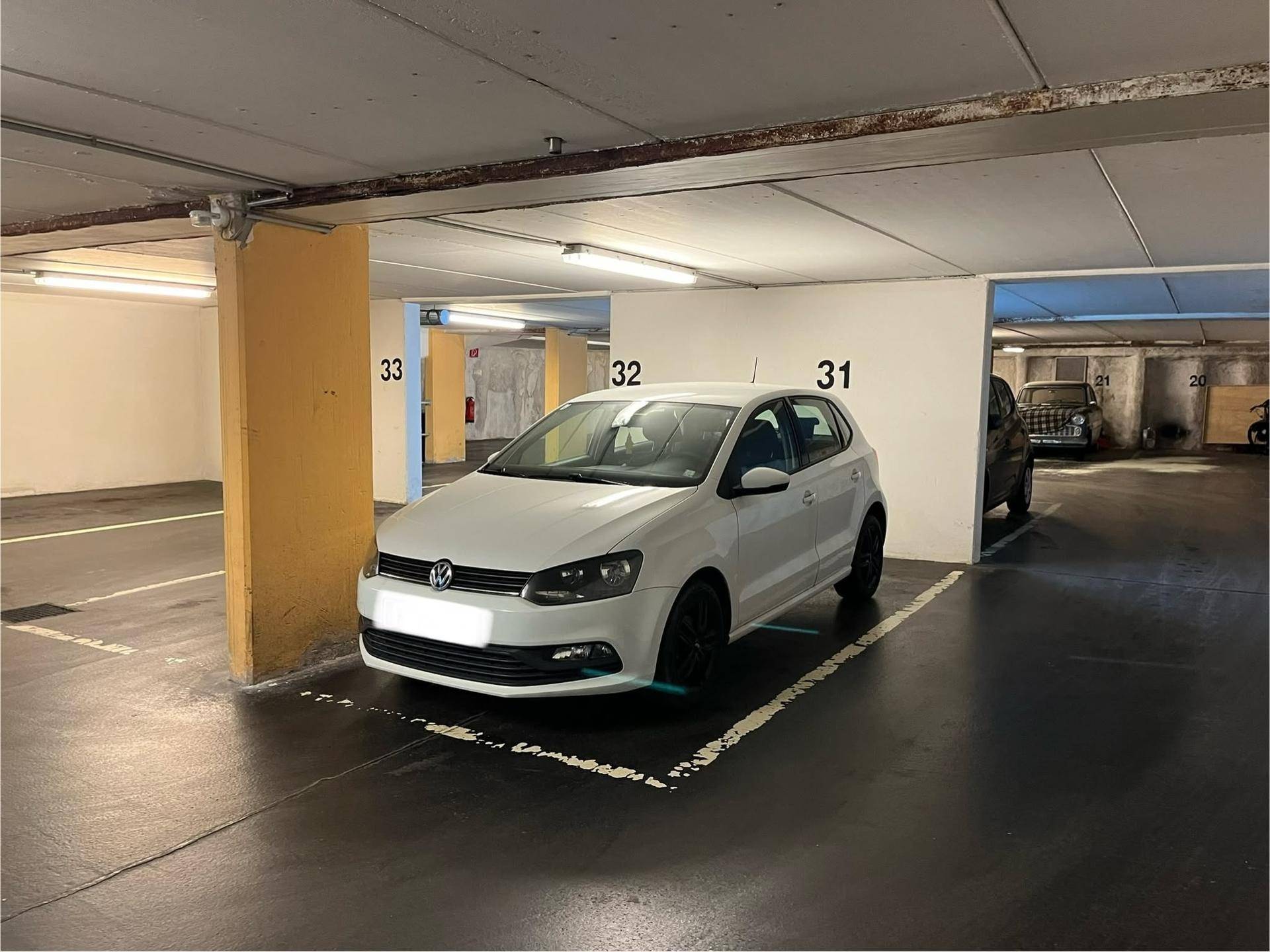 Heller Tiefgaragenstellplatz mit einem weißen Kleinwagen, gut beleuchtet und sauber gehalten.