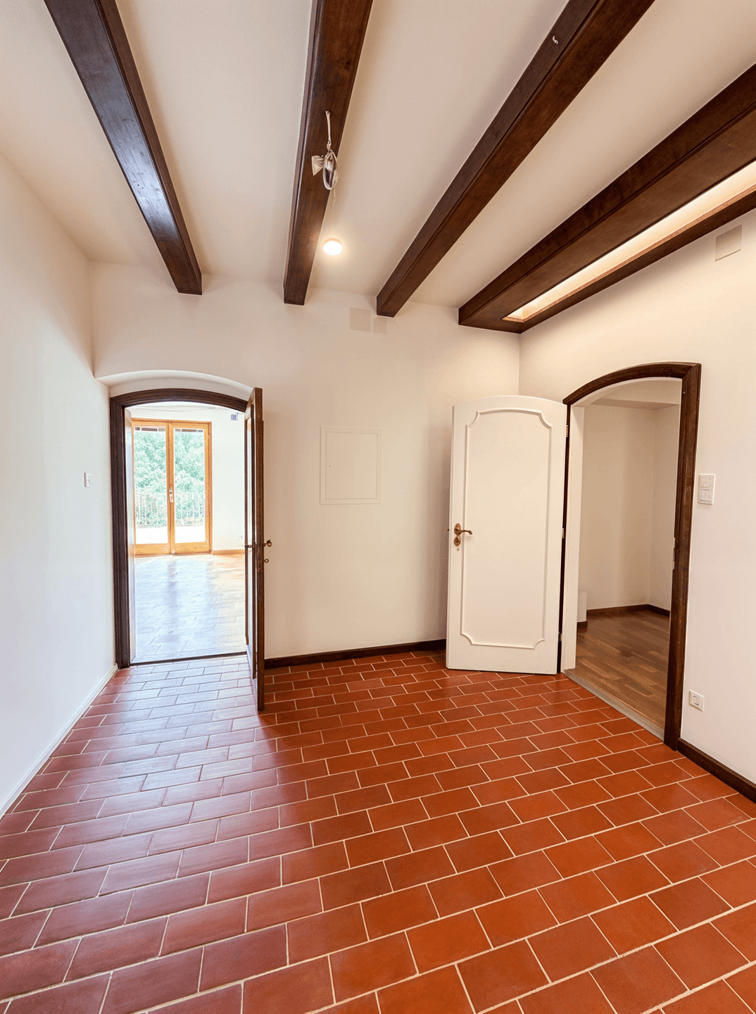 Rustikaler Raum mit Terrakotta-Fliesenboden und sichtbaren Holzbalken an der Decke.