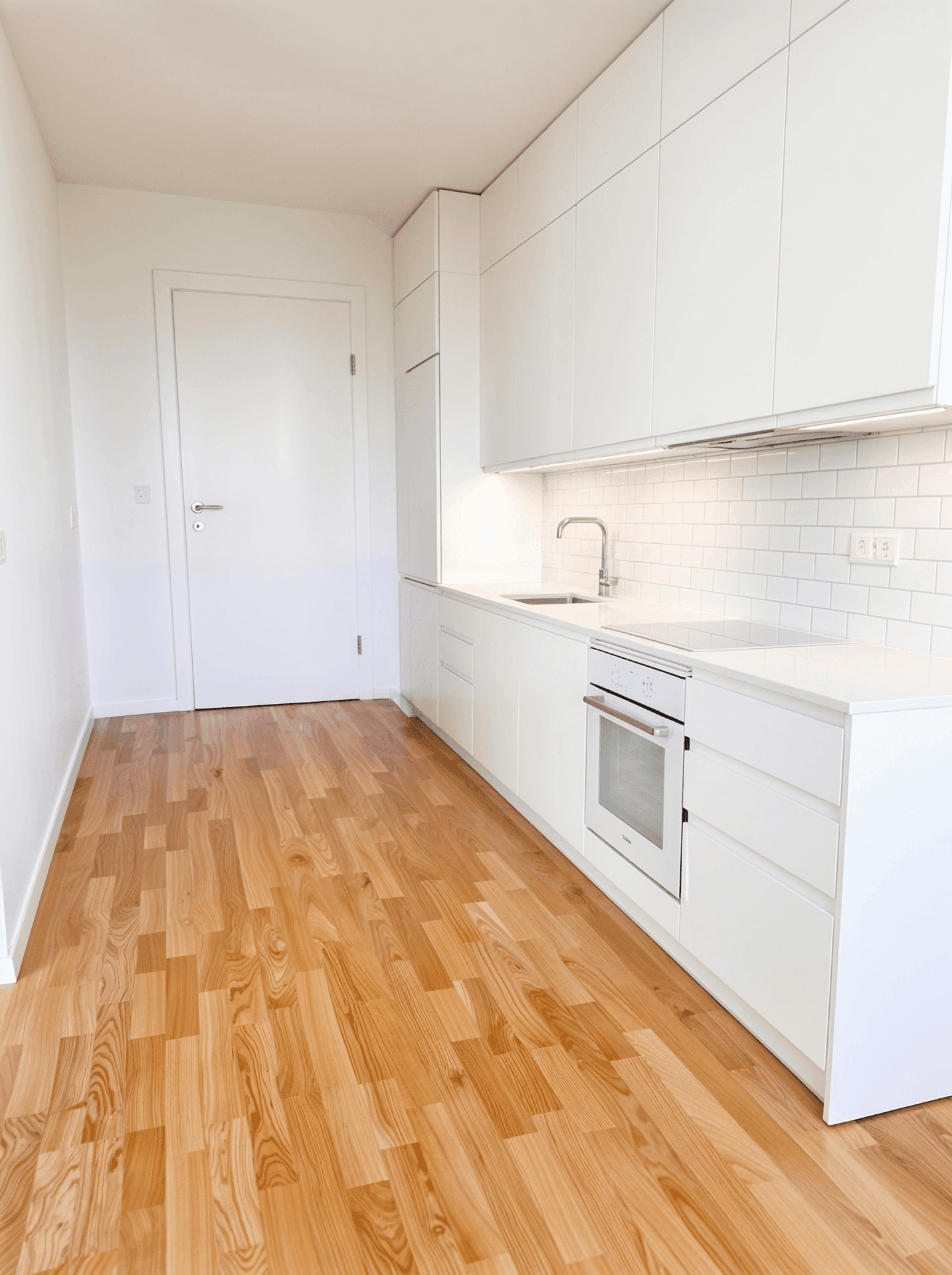 Moderne, weiße Einbauküche mit integrierten Geräten, hellem Holzboden und minimalistischem Design.