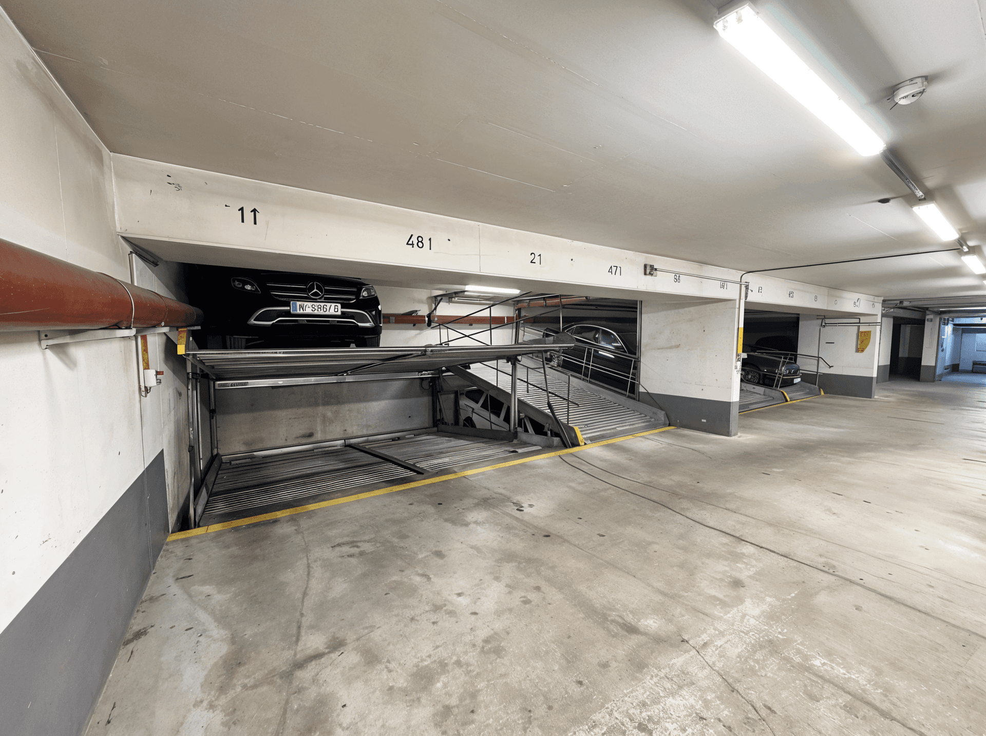 Übersicht einer Tiefgarage mit mehreren Autohebebühnen und hellen Leuchtstoffröhren.