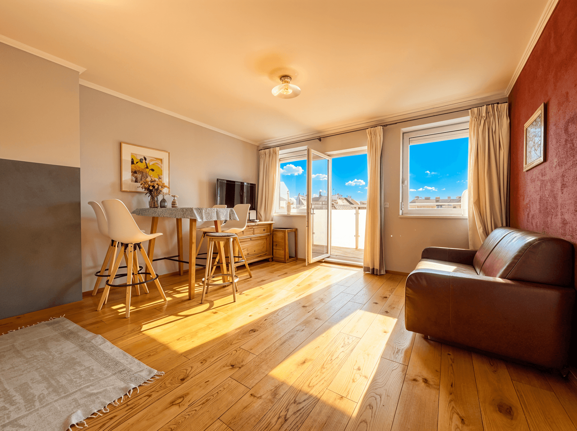 Lichtdurchfluteter Wohn-Essbereich mit Holzboden, Ledersofa und Zugang zum Balkon.