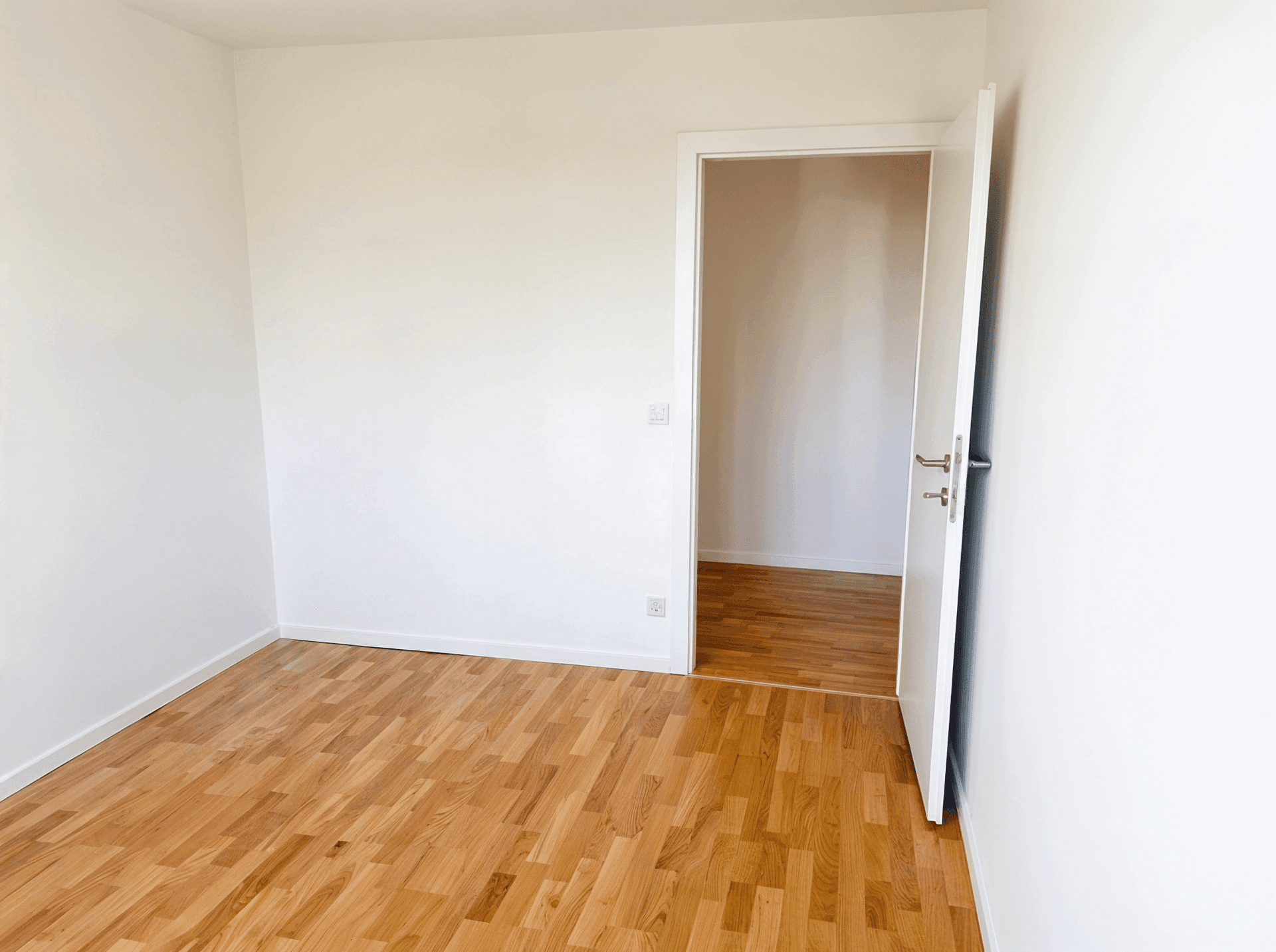 Leeres Zimmer mit Parkettboden und weiß gestrichenen Wänden, ideal für Schlaf- oder Arbeitszimmer.