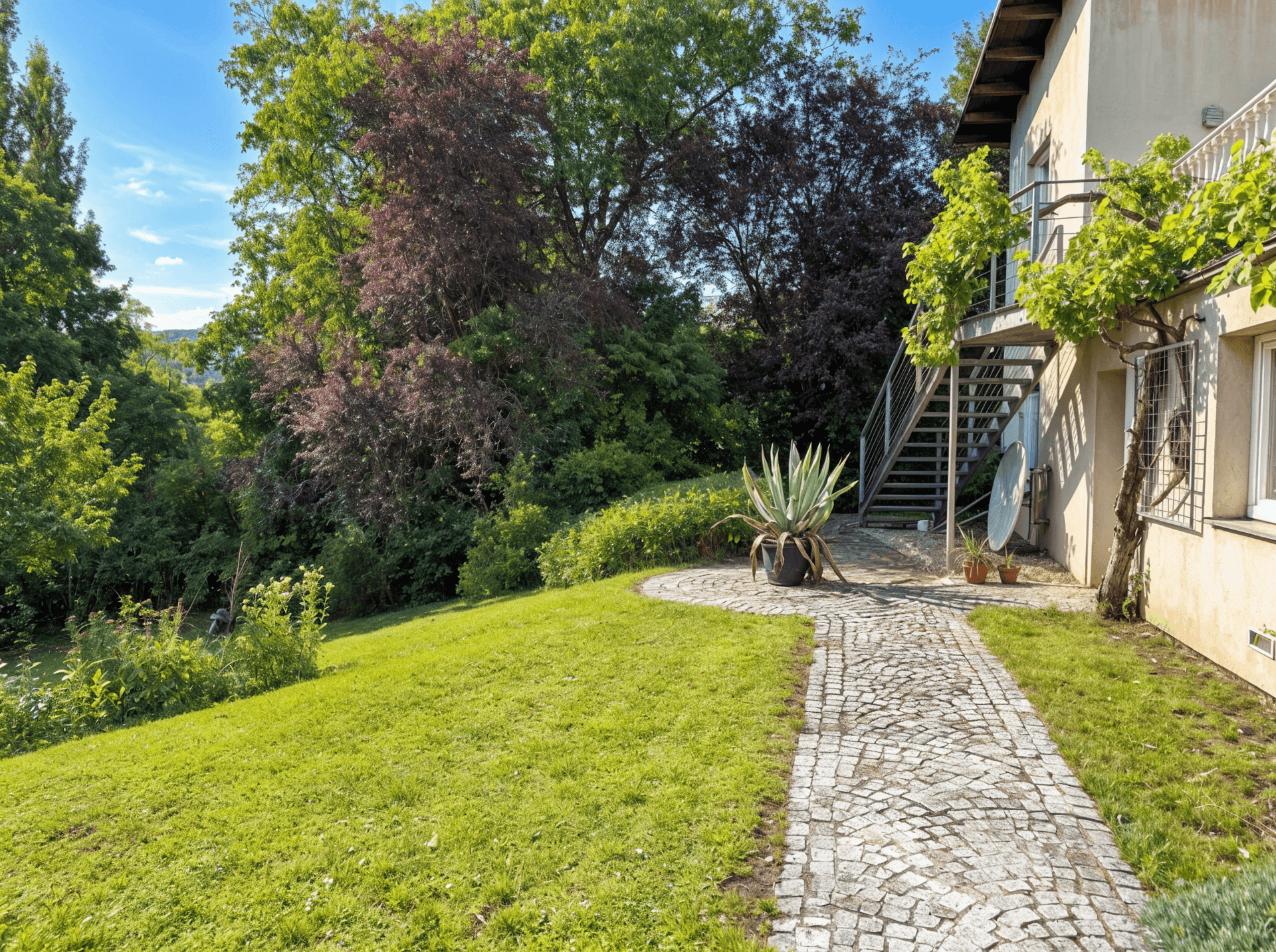 Geschwungener Gartenweg aus Kopfsteinpflaster, umgeben von Rasen und üppigen Pflanzen.