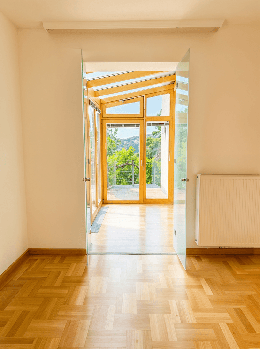 Heller Übergangsbereich mit Glaswänden und Holzelementen, der zu einem Wintergarten führt.