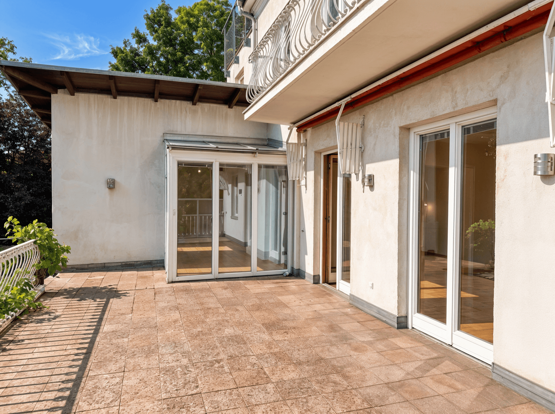 Geräumige Terrasse mit Zugang zum Haus und einem Wintergarten, umgeben von viel Grün.