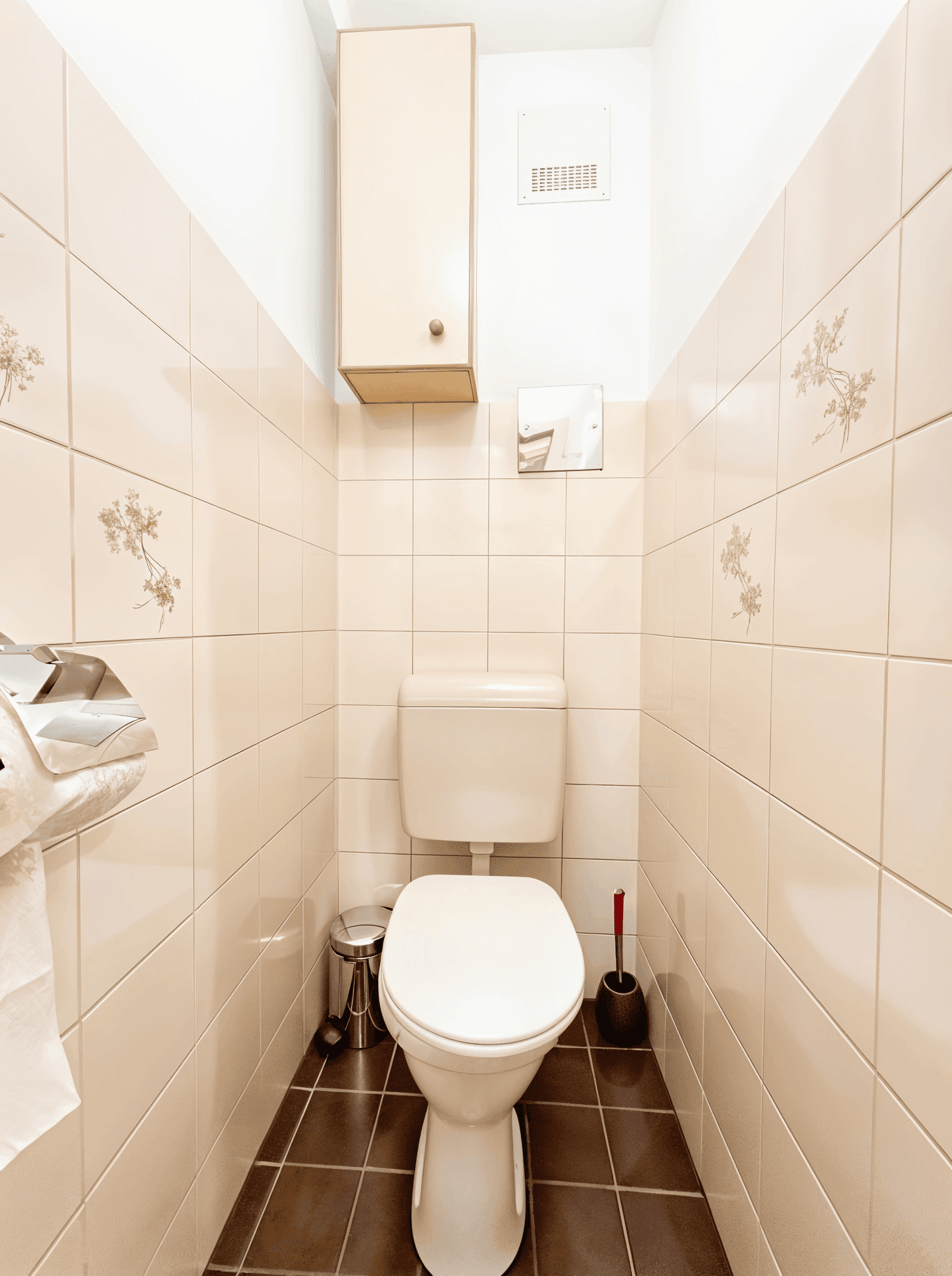 Separates WC mit Toilette, kleinem Waschbecken und Fliesen in Beige und Braun.