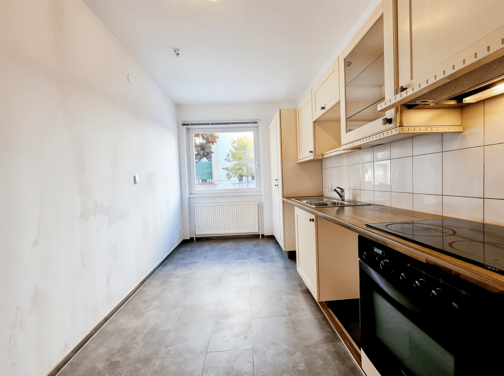 Leere Küche mit beigen Schränken, Holzarbeitsplatte und Fenster.