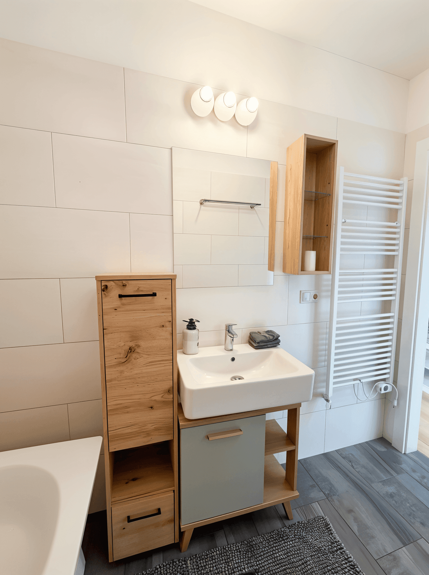 Helles Badezimmer mit modernem Waschbecken, beheiztem Handtuchhalter und Holzmöbeln.