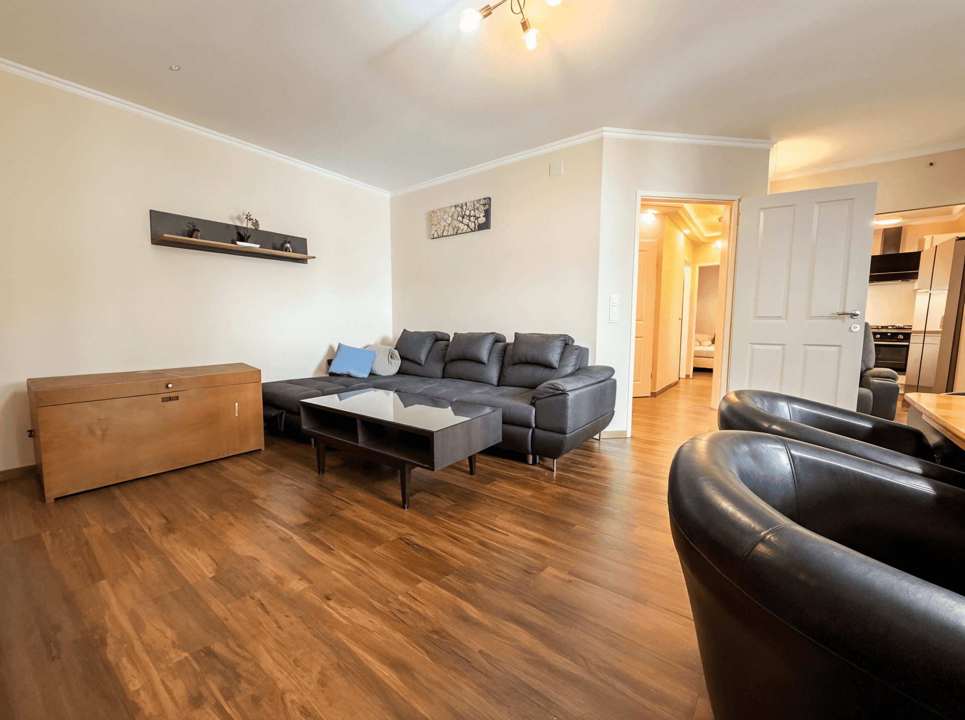 Gemütliches Wohnzimmer mit großem Sofa, Holzboden und Blick in die Küche.