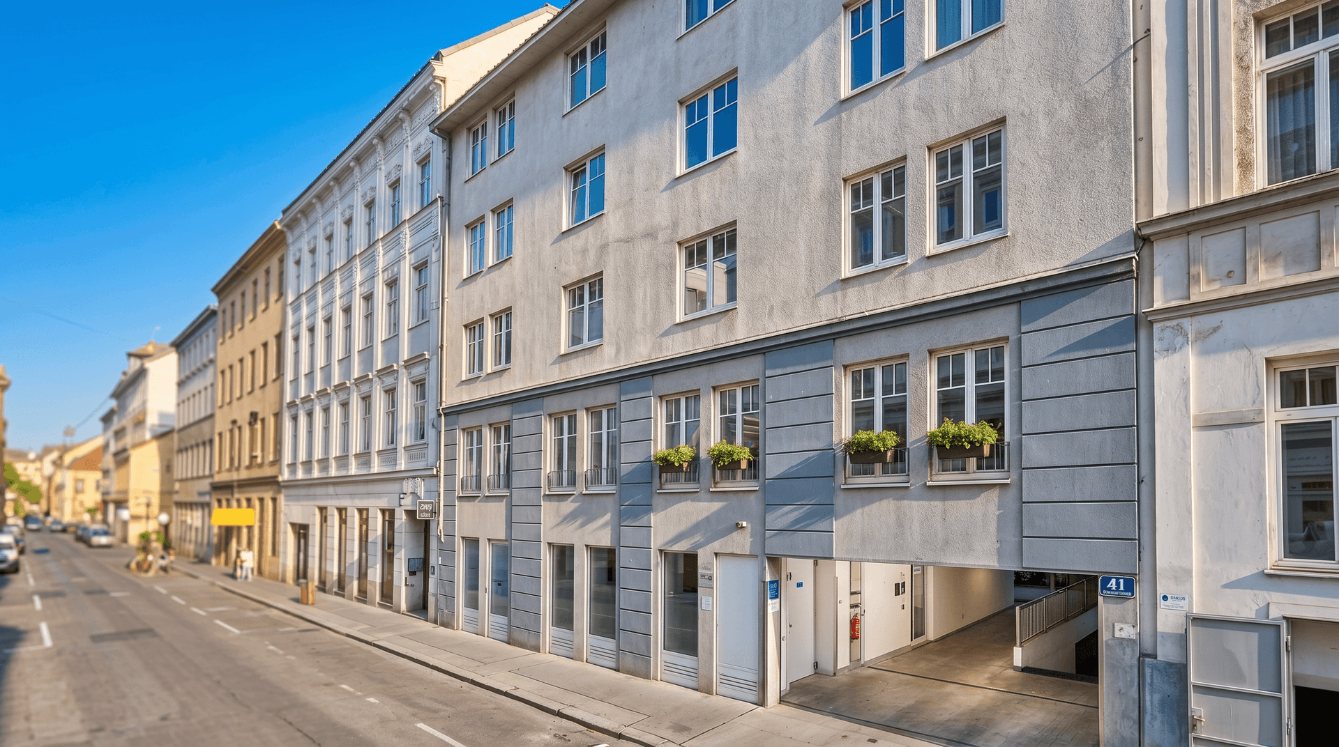 Fassade eines Mehrfamilienhauses an einer Stadtstraße mit integrierter Tiefgarageneinfahrt.