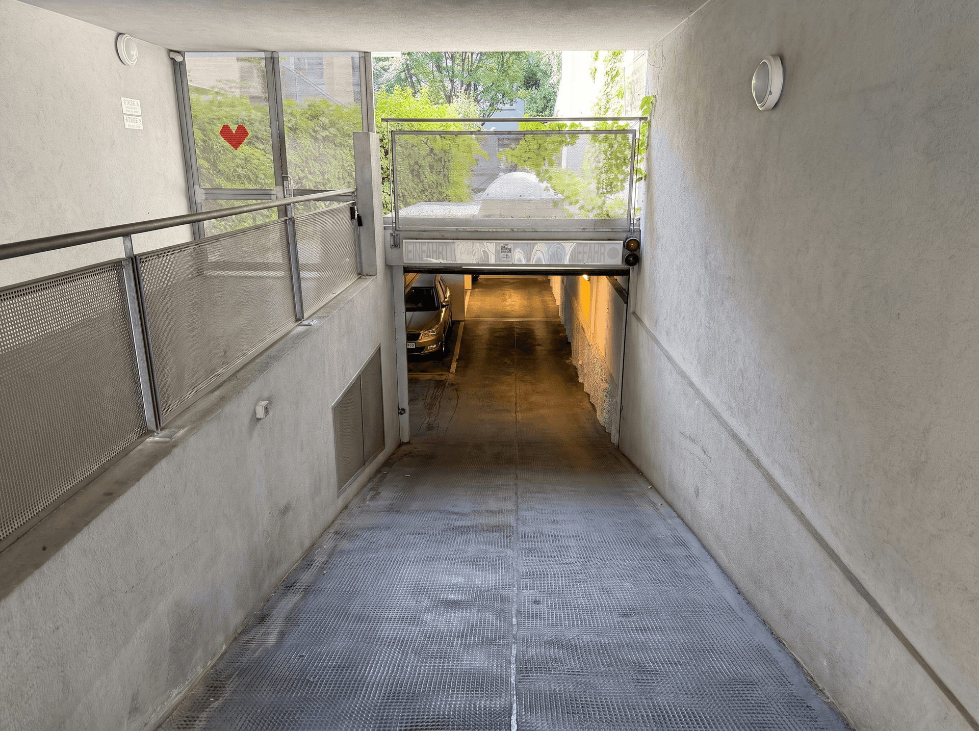 Einfahrt zu einer Tiefgarage mit Blick ins Freie und moderner Metallkonstruktion am Eingang.