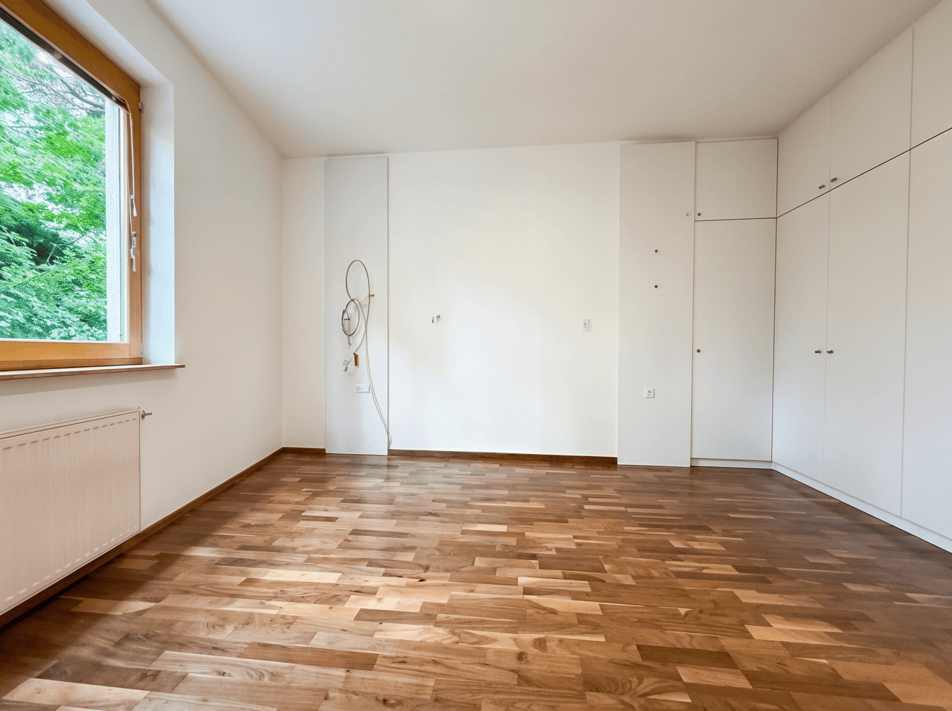 Helles Schlafzimmer mit Holzboden und praktischen Einbauschränken entlang einer Wand.