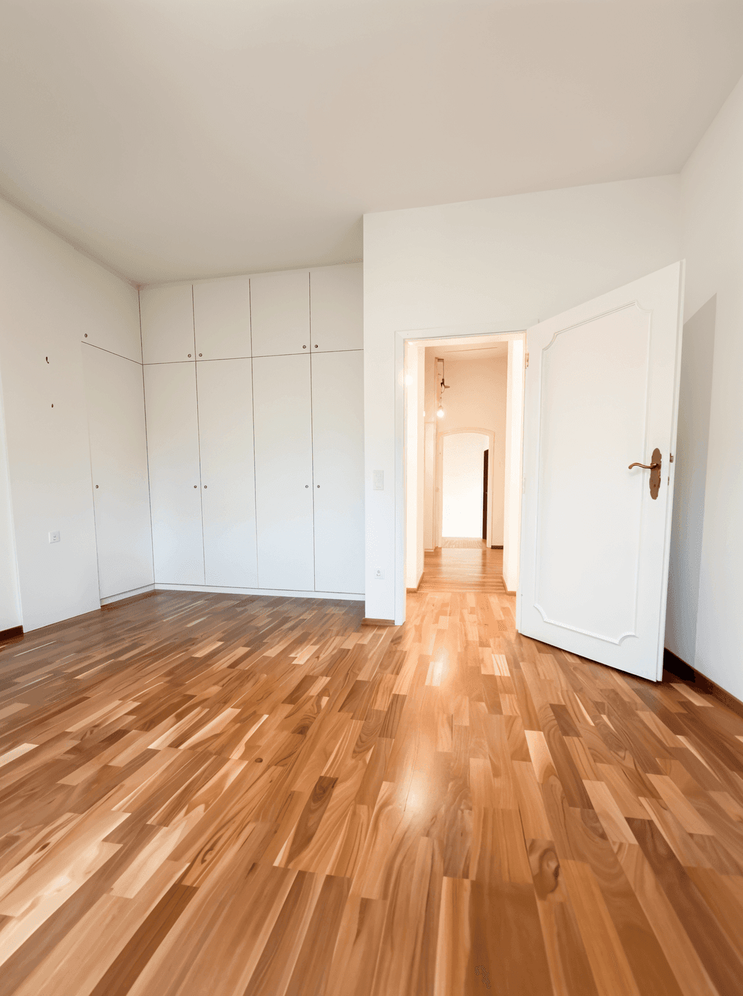 Geräumiges Schlafzimmer mit Holzboden und integrierten Wandschränken, gut beleuchtet.