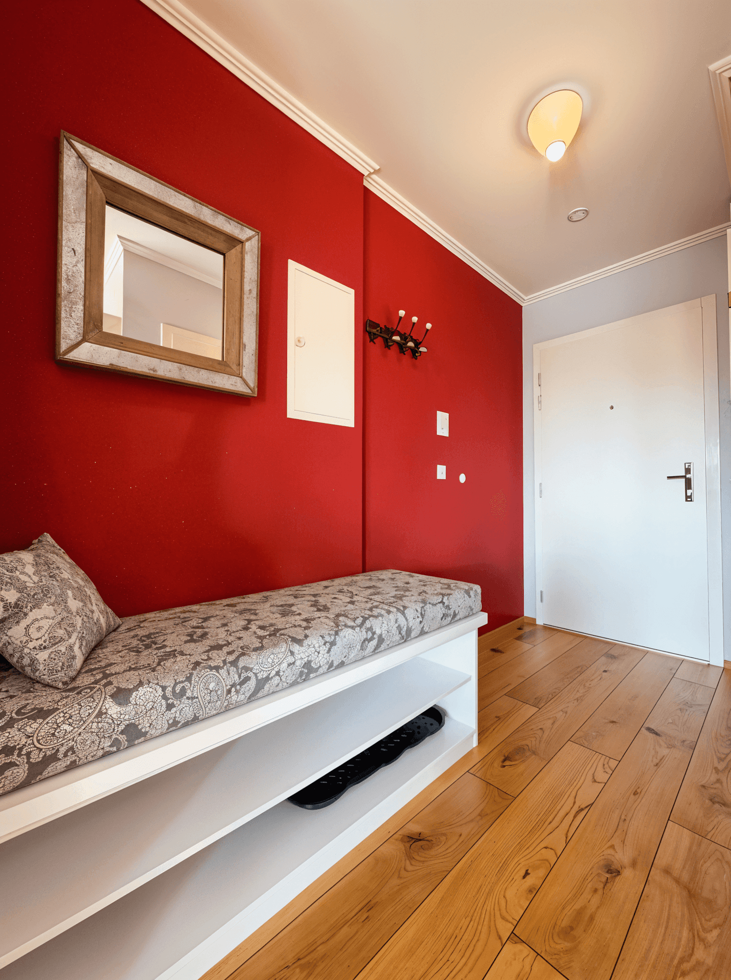 Eingangsbereich mit roter Akzentwand, Holzboden und einer Sitzbank mit Stauraum.