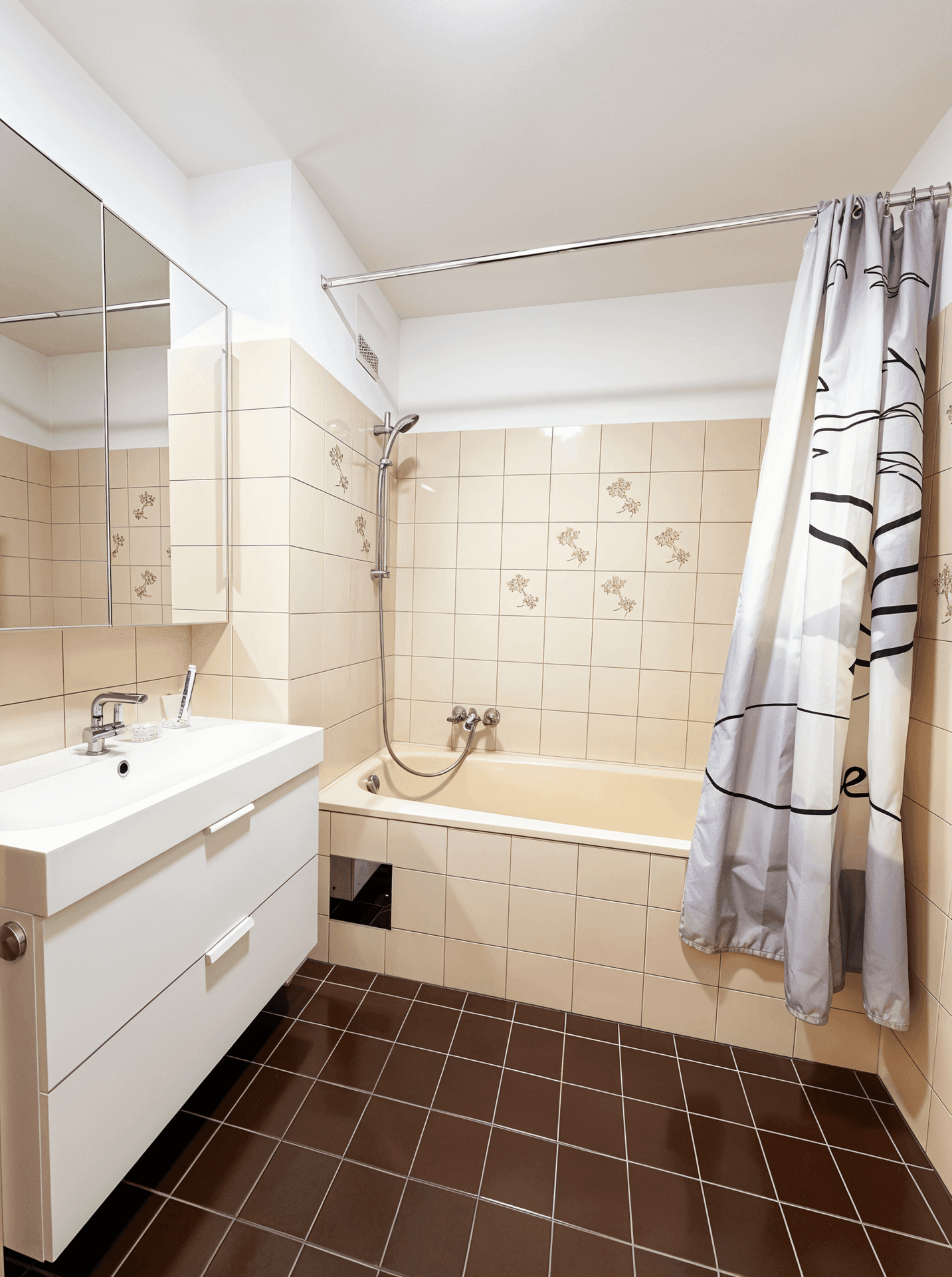 Badezimmer mit Badewanne, Waschbecken und Spiegelschrank in beigen und braunen Fliesen.