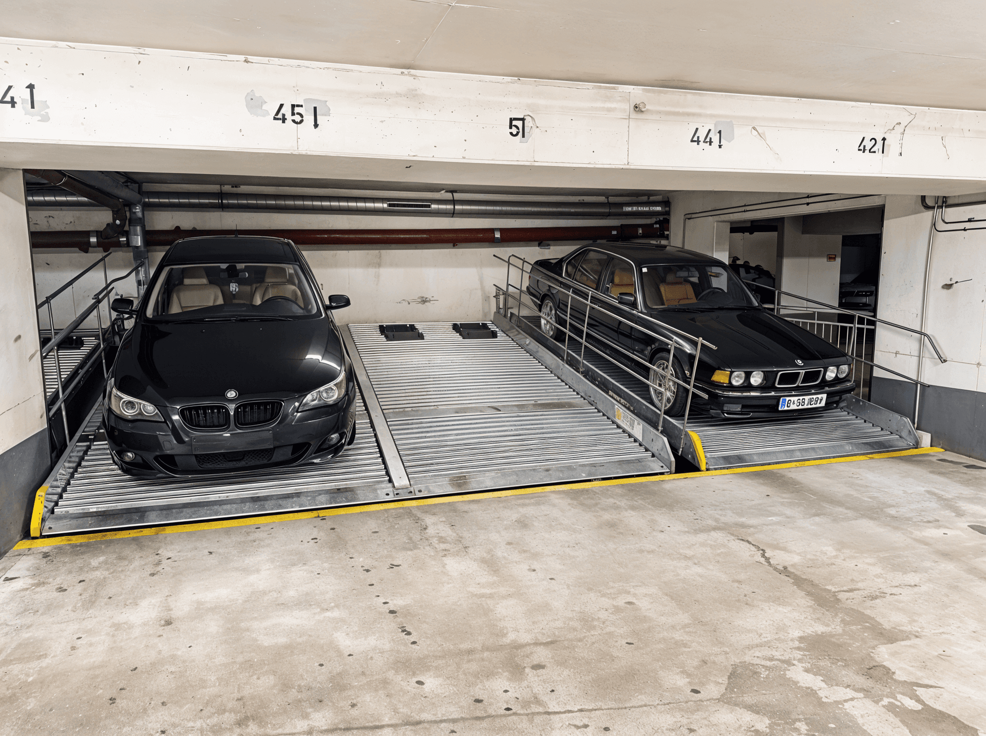 Zwei schwarze BMW-Limousinen auf den Parkhebebühnen einer modernen Tiefgarage.