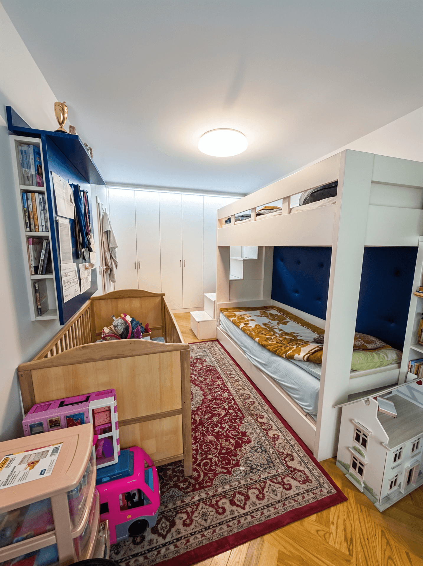 Kinderzimmer mit Etagenbett, Babybett und integrierten Schränken.