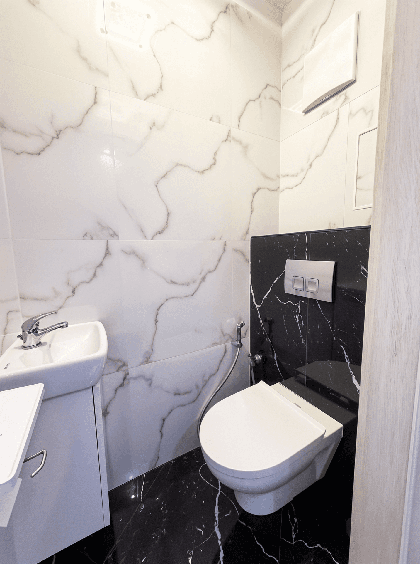 Gäste-WC mit wandhängender Toilette, kleinem Waschbecken und Marmorfliesen.