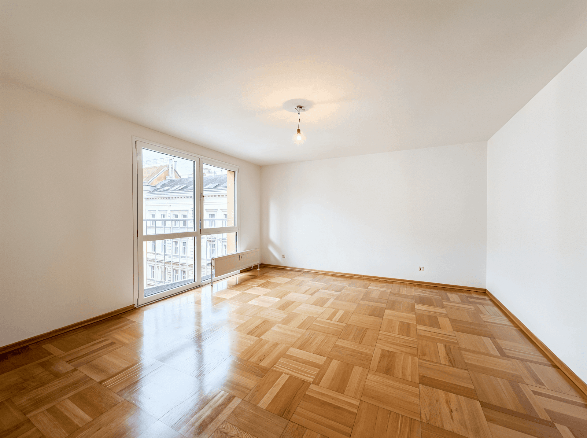 Helles, unmöbliertes Zimmer mit Parkettboden und großen Fenstern, die den Raum erhellen.