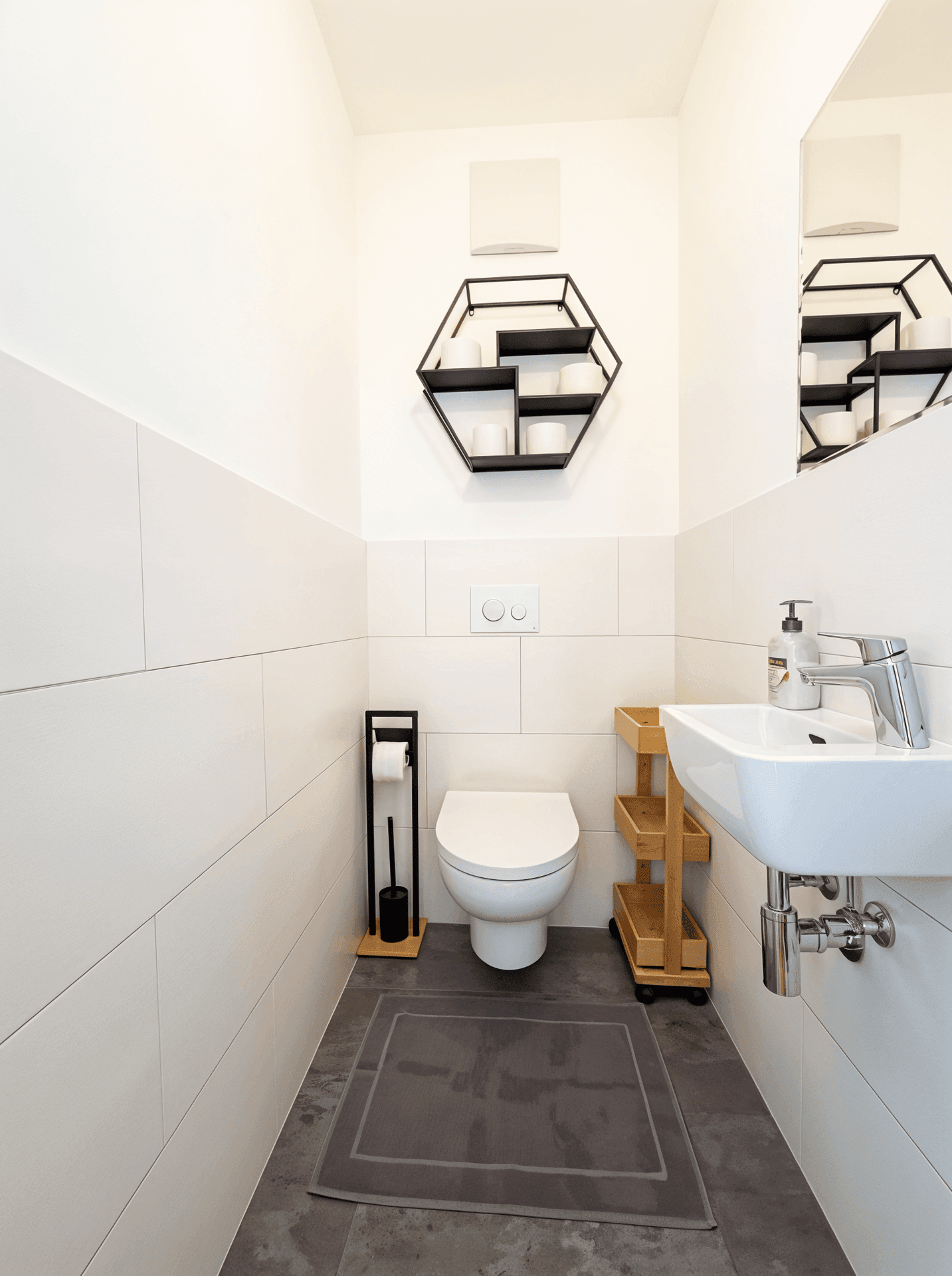 Modernes Gäste-WC mit wandhängender Toilette, kleinem Waschbecken und weißen Fliesen.