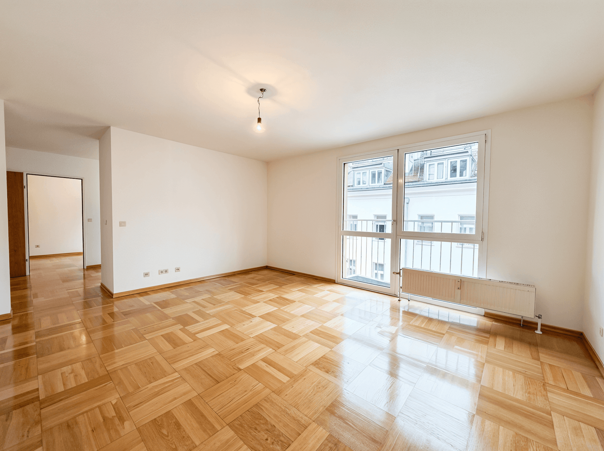 Geräumiges, leeres Zimmer mit Parkettboden und großen Fenstern, die viel Tageslicht bieten.