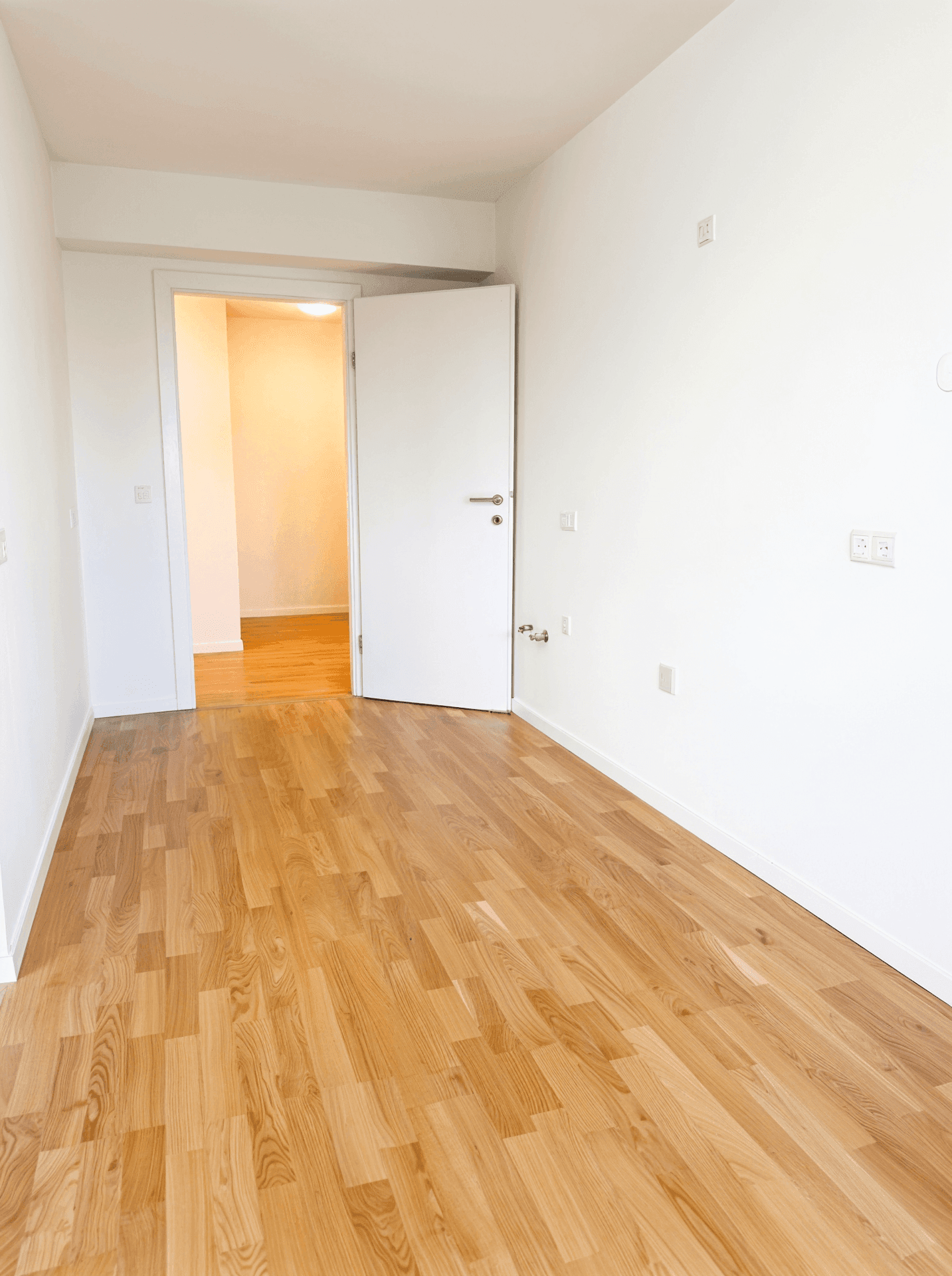 Leeres Zimmer mit hellem Parkettboden und weiß gestrichenen Wänden, bereit zur individuellen Einrichtung.