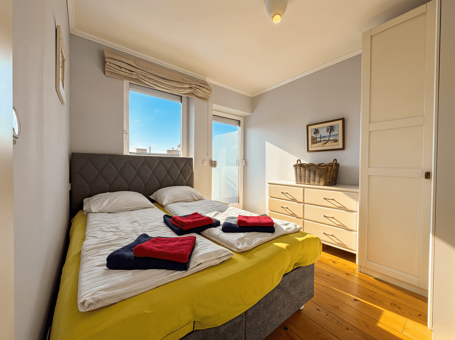 Helles Schlafzimmer mit zwei Einzelbetten, Holzfußboden und Zugang zum Balkon.