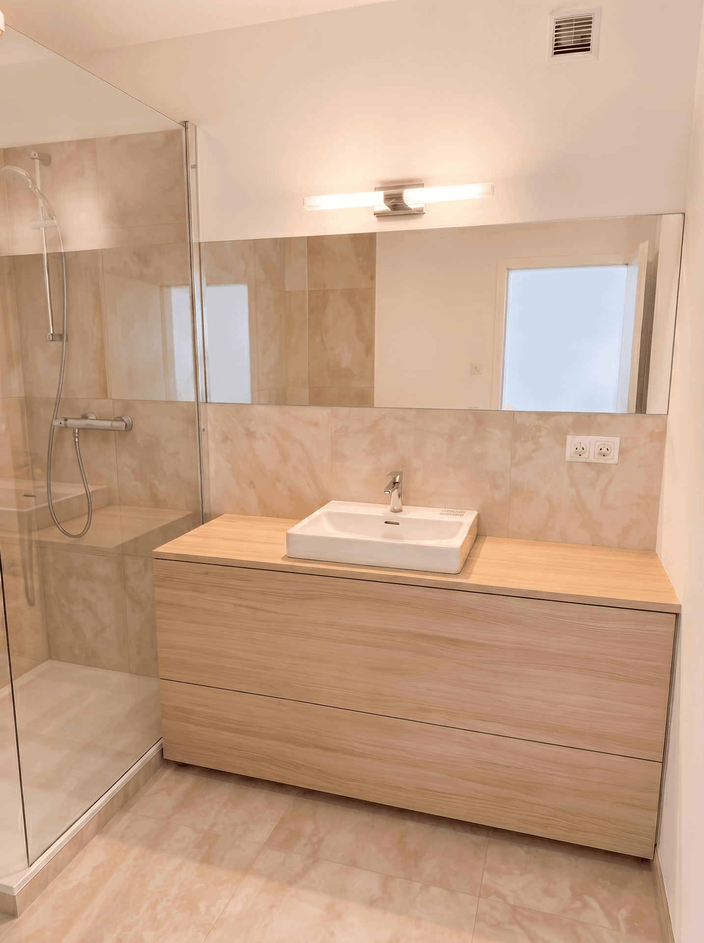 Modernes Badezimmer mit Waschtisch, großem Spiegel und begehbarer Dusche, elegant gefliest.