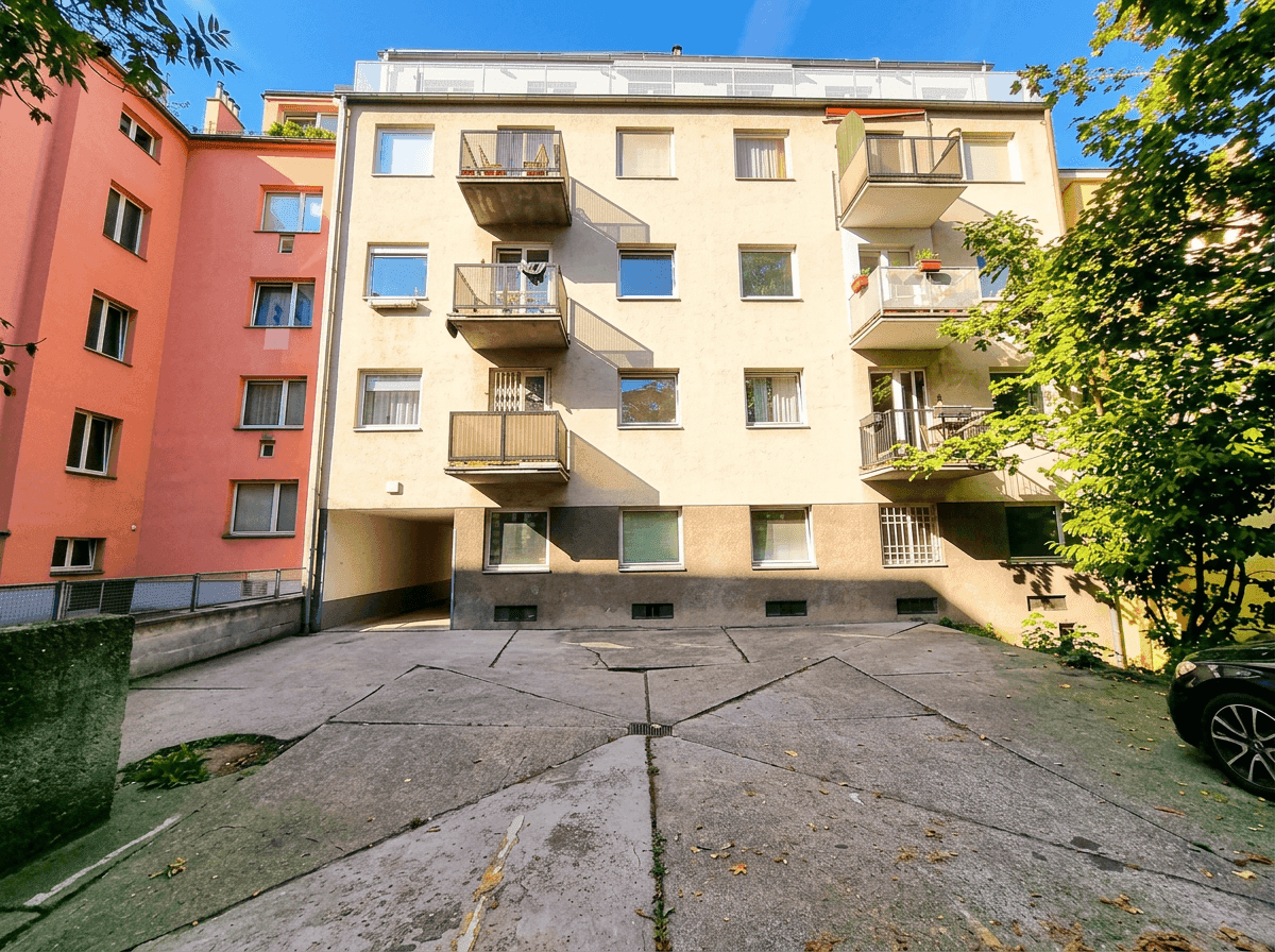 Rückseite eines Mehrfamilienhauses mit Balkonen und einem gepflasterten Hof.