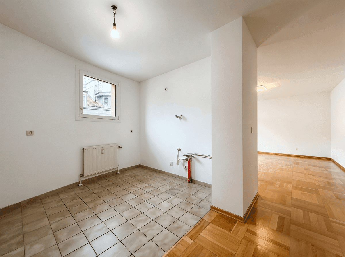 Leerer Küchenbereich mit Fliesenboden und Anschlüssen für eine zukünftige Einbauküche.