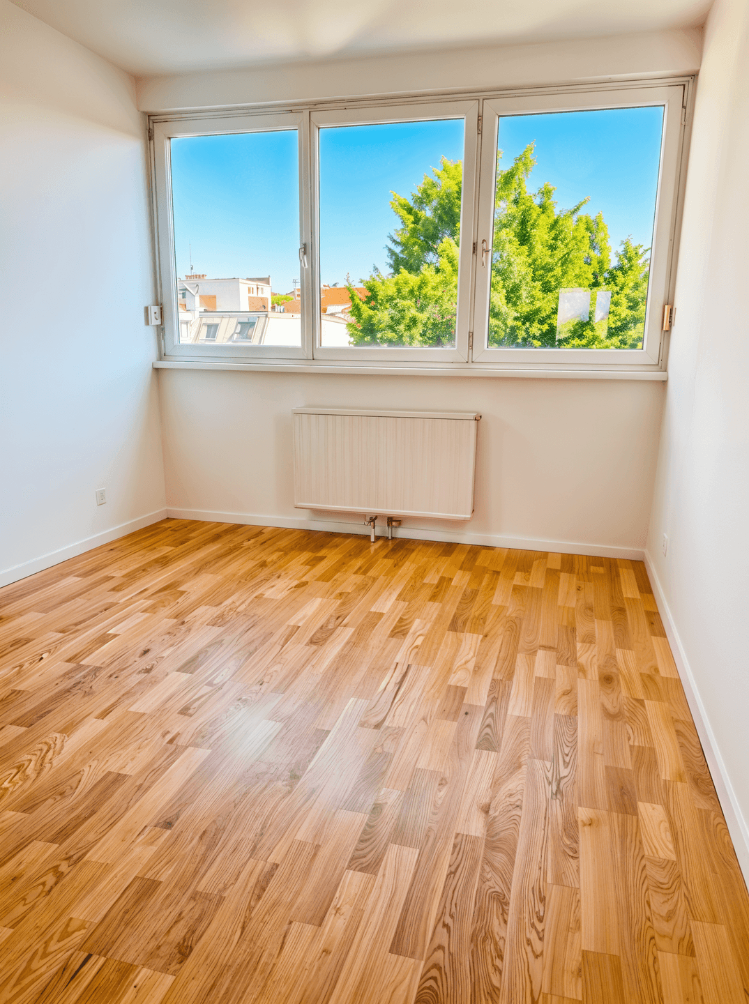 Heller, leerer Raum mit Holzboden und großen Fenstern mit Blick ins Grüne.