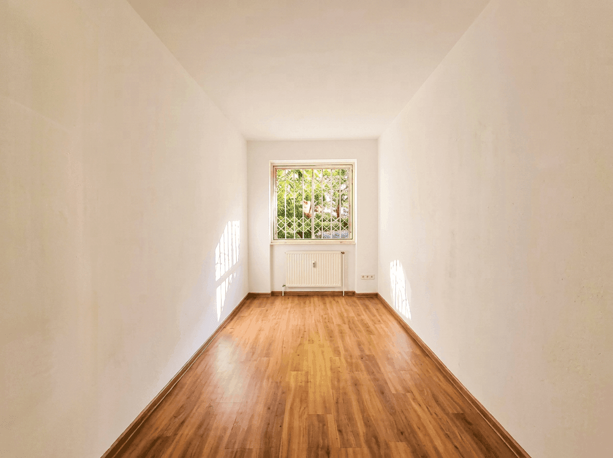 Leeres Schlafzimmer mit Holzboden und Fenster, das viel Licht hereinlässt.