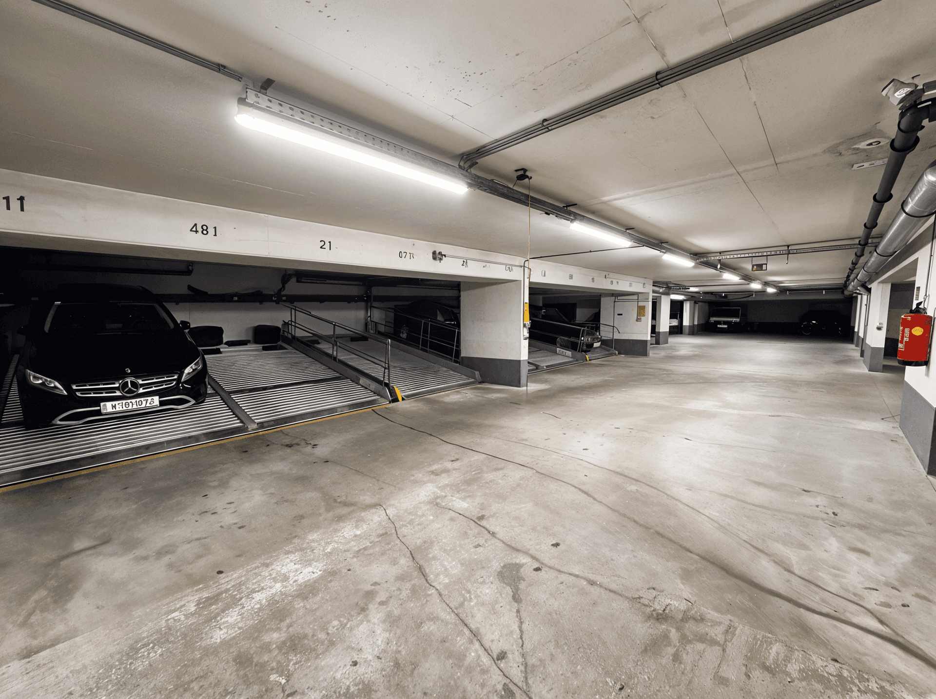 Geräumige Tiefgarage mit mehreren Autohebebühnen und Betonboden.