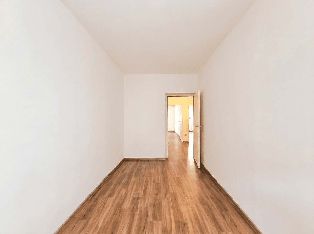 Leeres Schlafzimmer mit Holzboden und Zugang zu einem weiteren Raum.