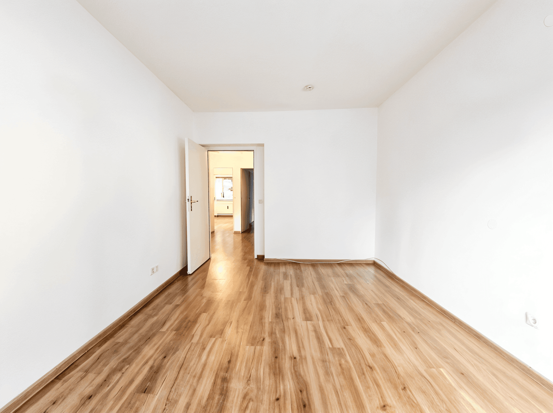 Leeres Wohnzimmer mit Holzboden und Zugang zu einem weiteren Raum.