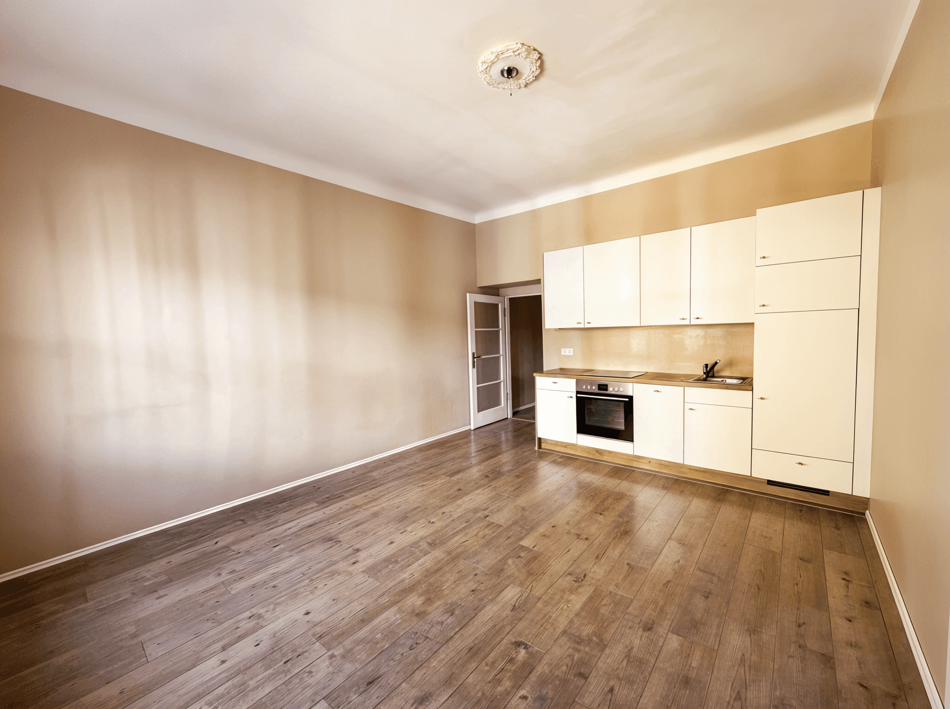 Heller, unmöblierter Raum mit installierter Küchenzeile, Holzboden und Zugang zu einem weiteren Zimmer.