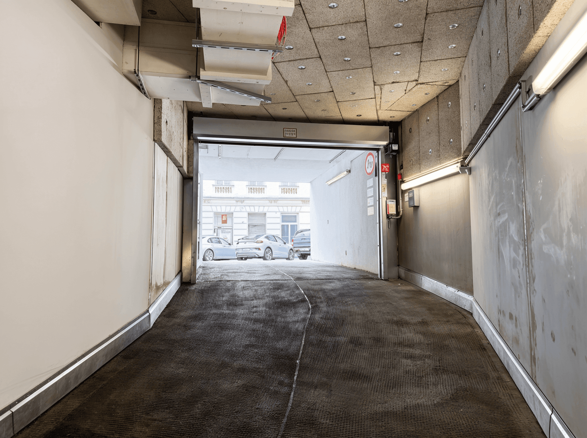 Ausfahrtrampe einer Tiefgarage, die auf eine belebte Stadtstraße mit parkenden Autos führt.