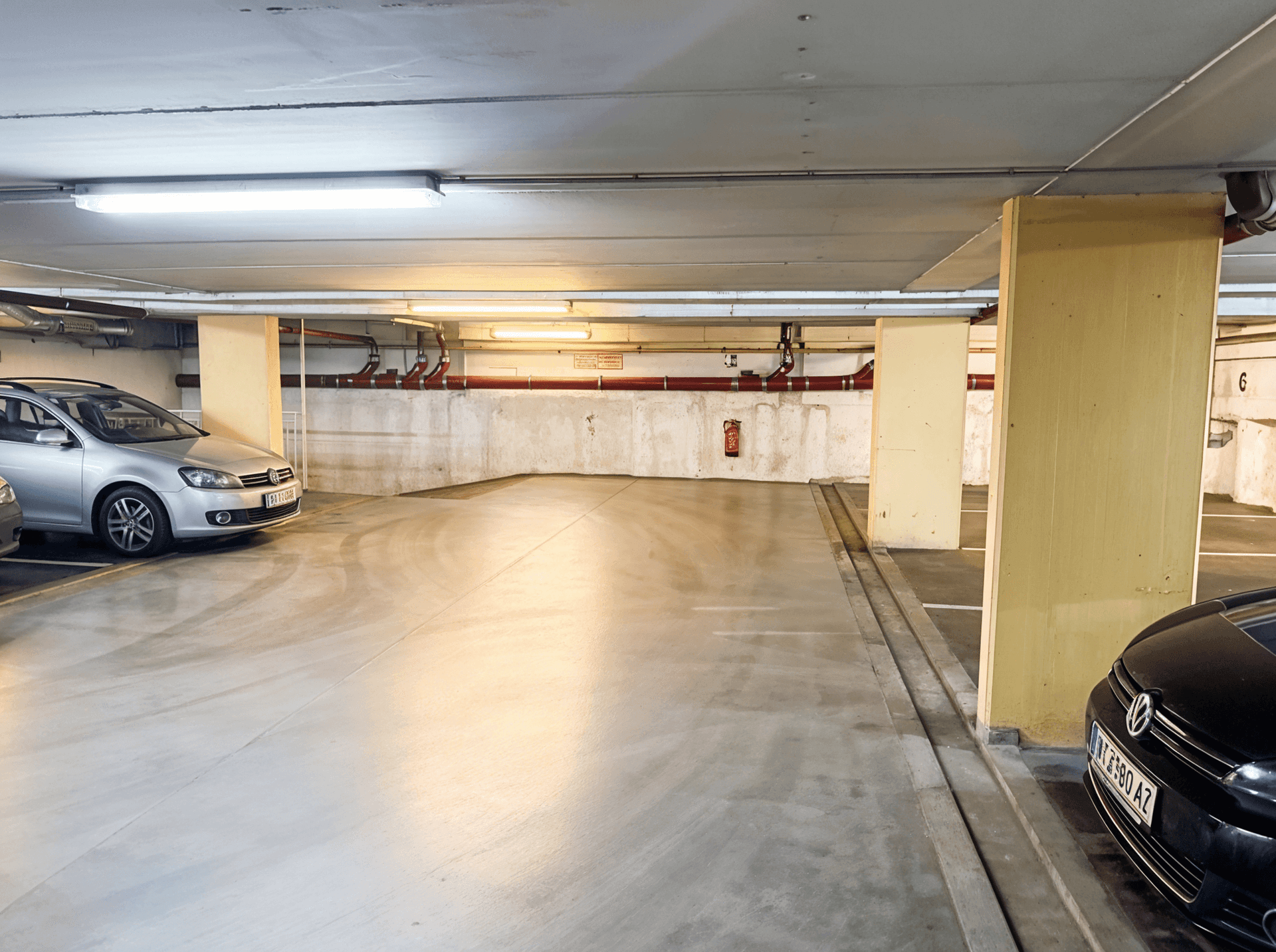 Weitläufiger Bereich einer Tiefgarage mit weiteren Stellplätzen und einer Rampe im Hintergrund.