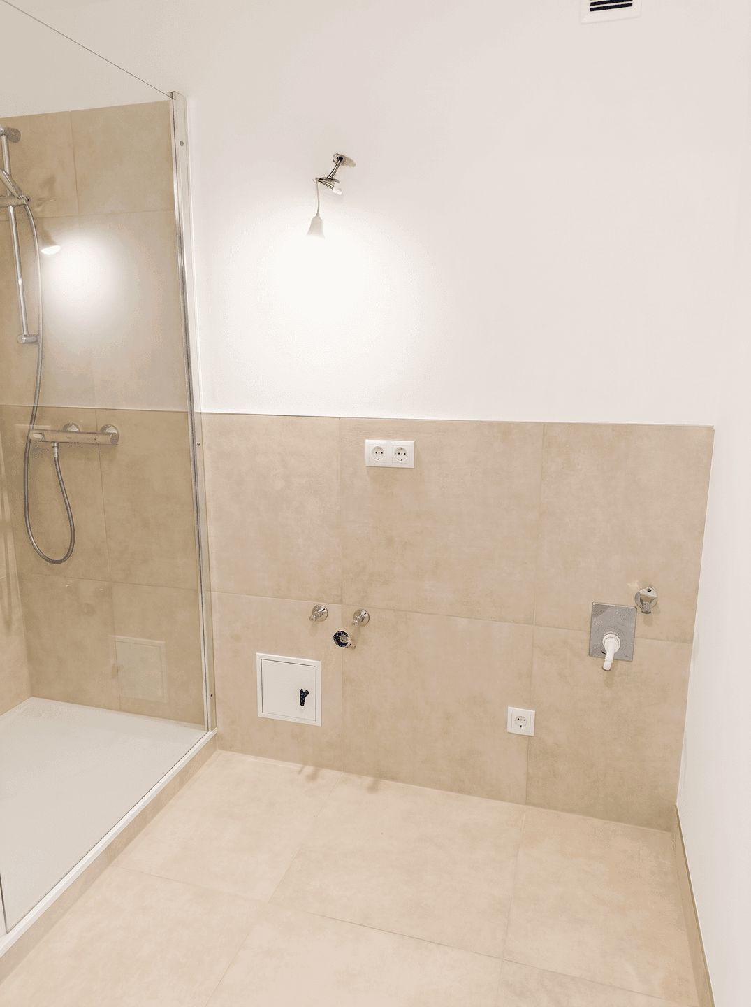 Badezimmer im Rohbau mit Duschbereich und Anschlüssen für Waschtisch und WC.