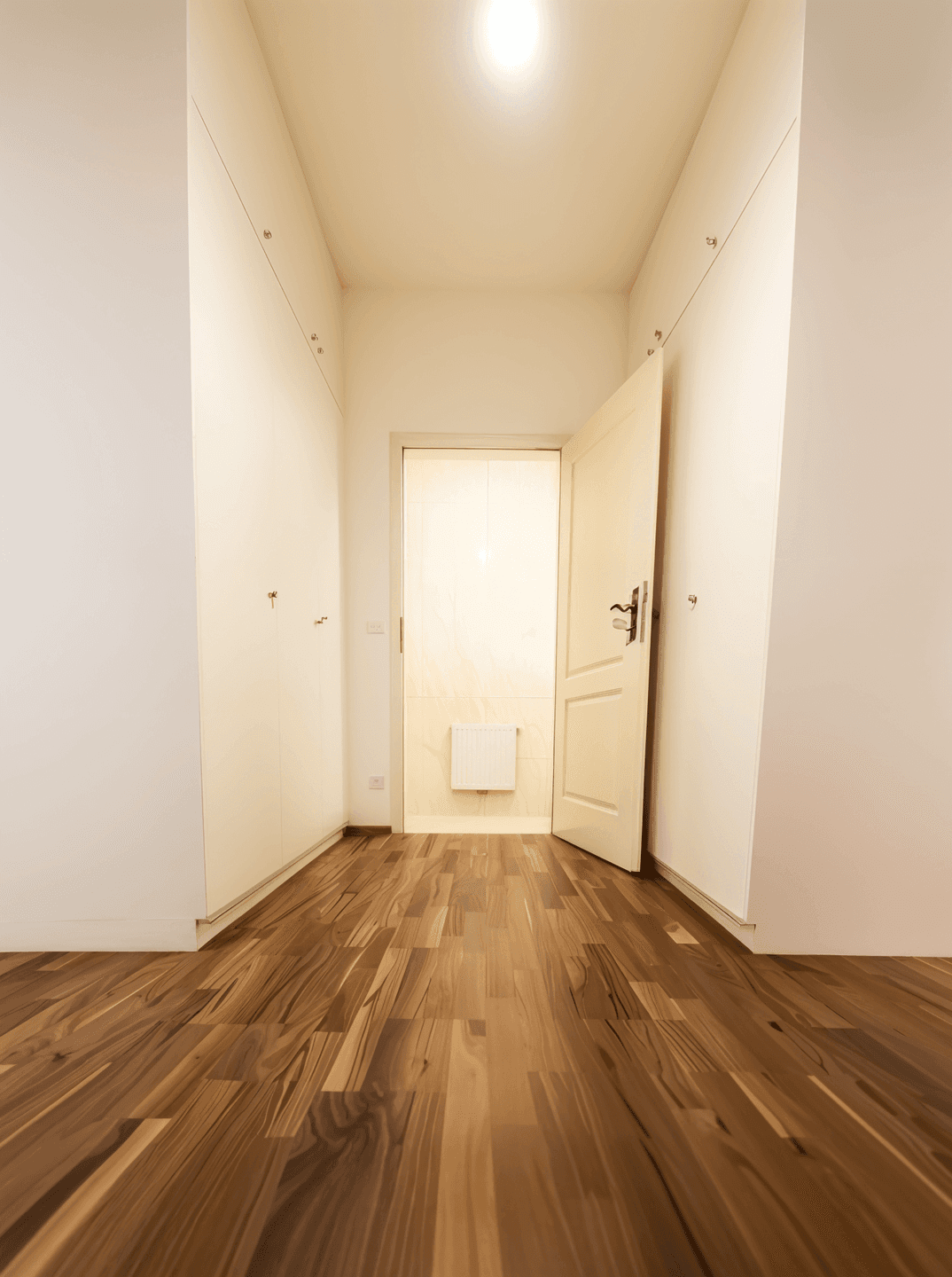 Begehbarer Kleiderschrank mit Holzboden und integrierten Schränken, der zu einem weiteren Raum führt.