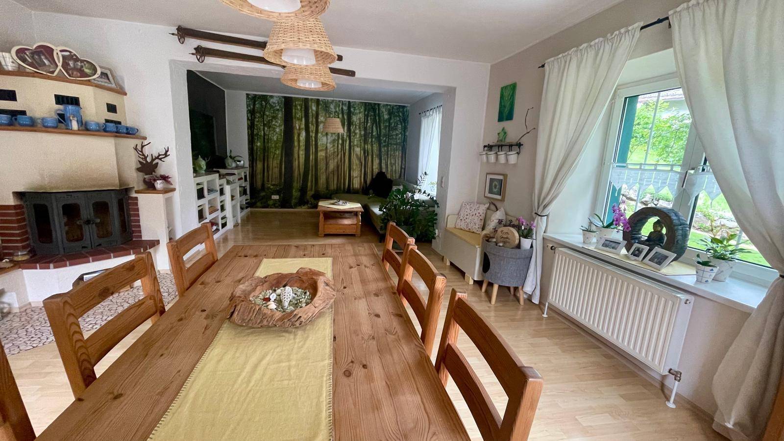 Rustikaler Essbereich mit Holztisch und Kamin, offen zum Wohnzimmer mit Waldtapete.