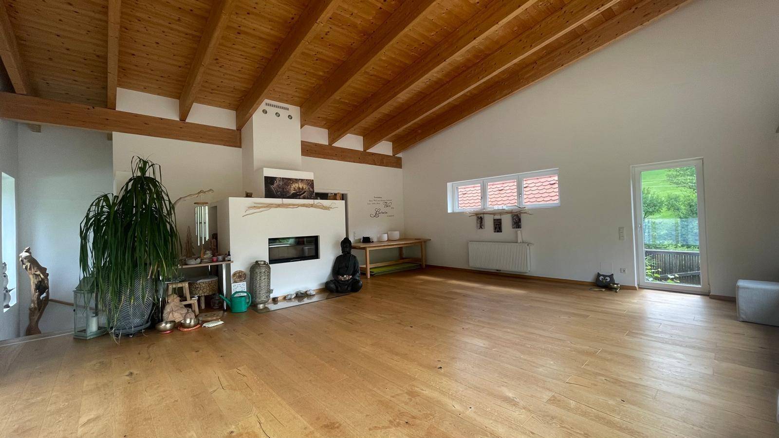 Großzügiger Wohnraum mit hoher Holzdecke, Kamin und Blick ins Grüne.