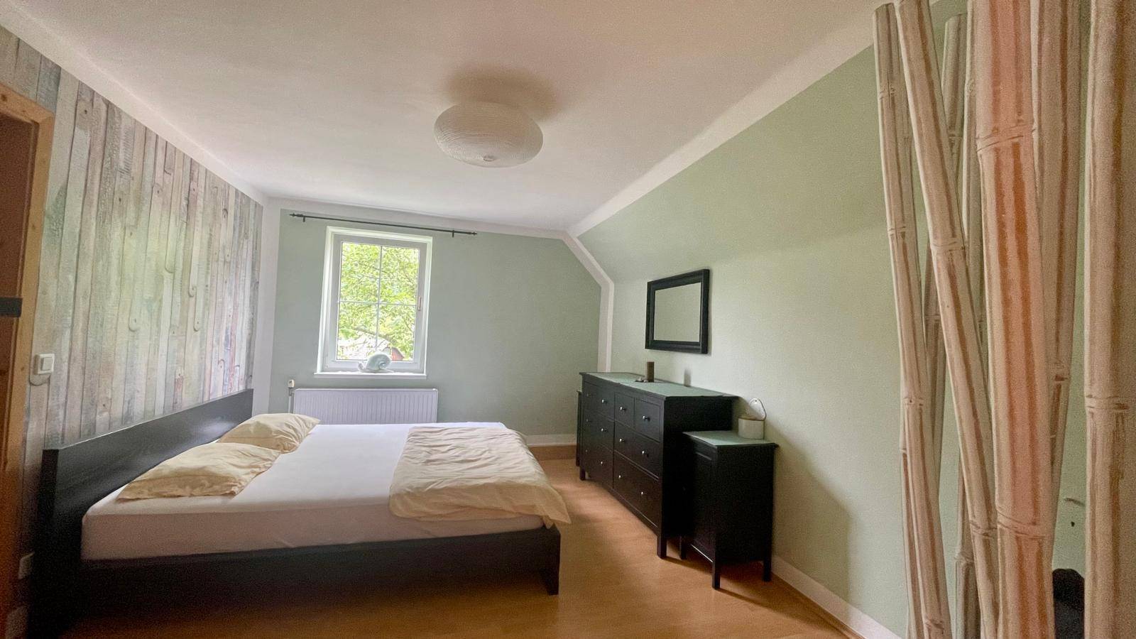 Gemütliches Schlafzimmer mit Holzwand, grün gestrichenen Wänden und einem großen Doppelbett.