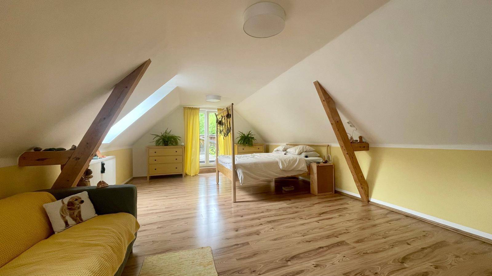 Geräumiges Schlafzimmer im Dachgeschoss mit Holzbalken, Laminatboden und Zugang zum Balkon.