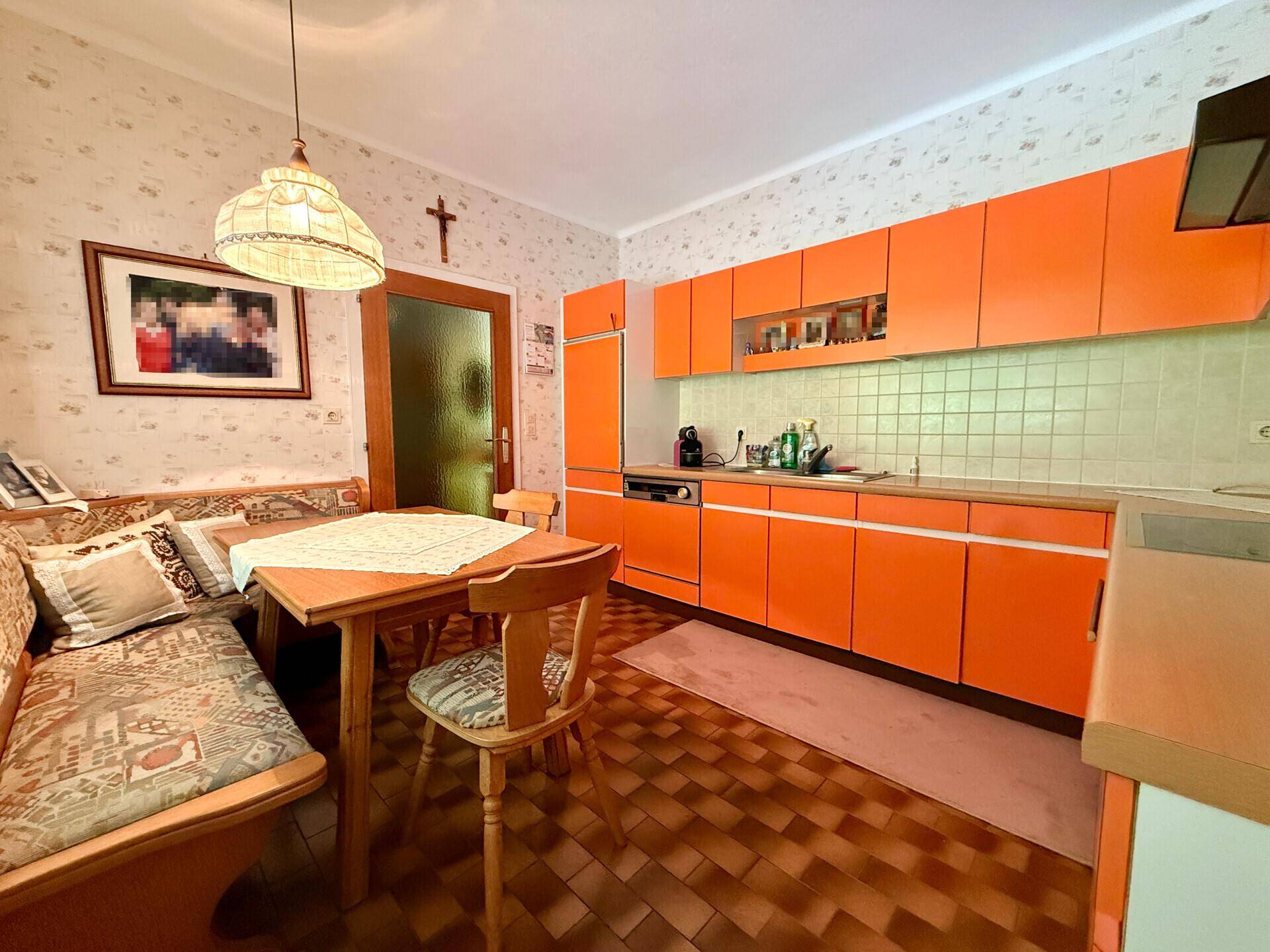 Küche mit orangefarbenen Schränken, Essbereich und Fliesenboden im traditionellen Stil.