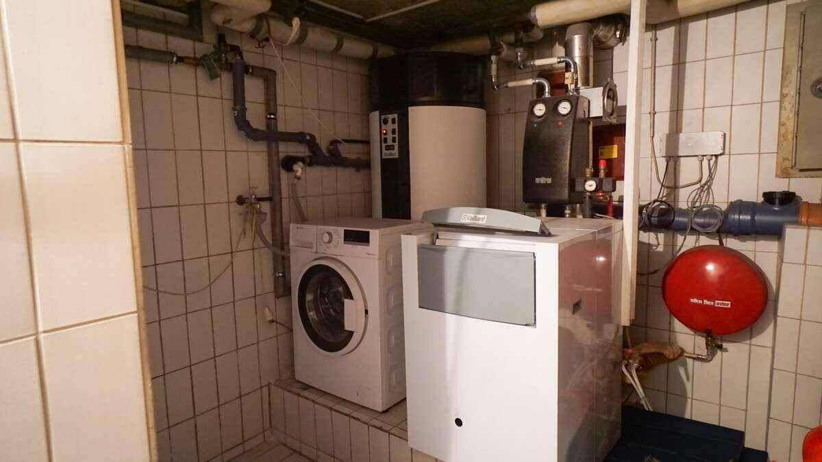 Technikraum im Keller mit Heizungsanlage, Waschmaschine und Fliesenboden.