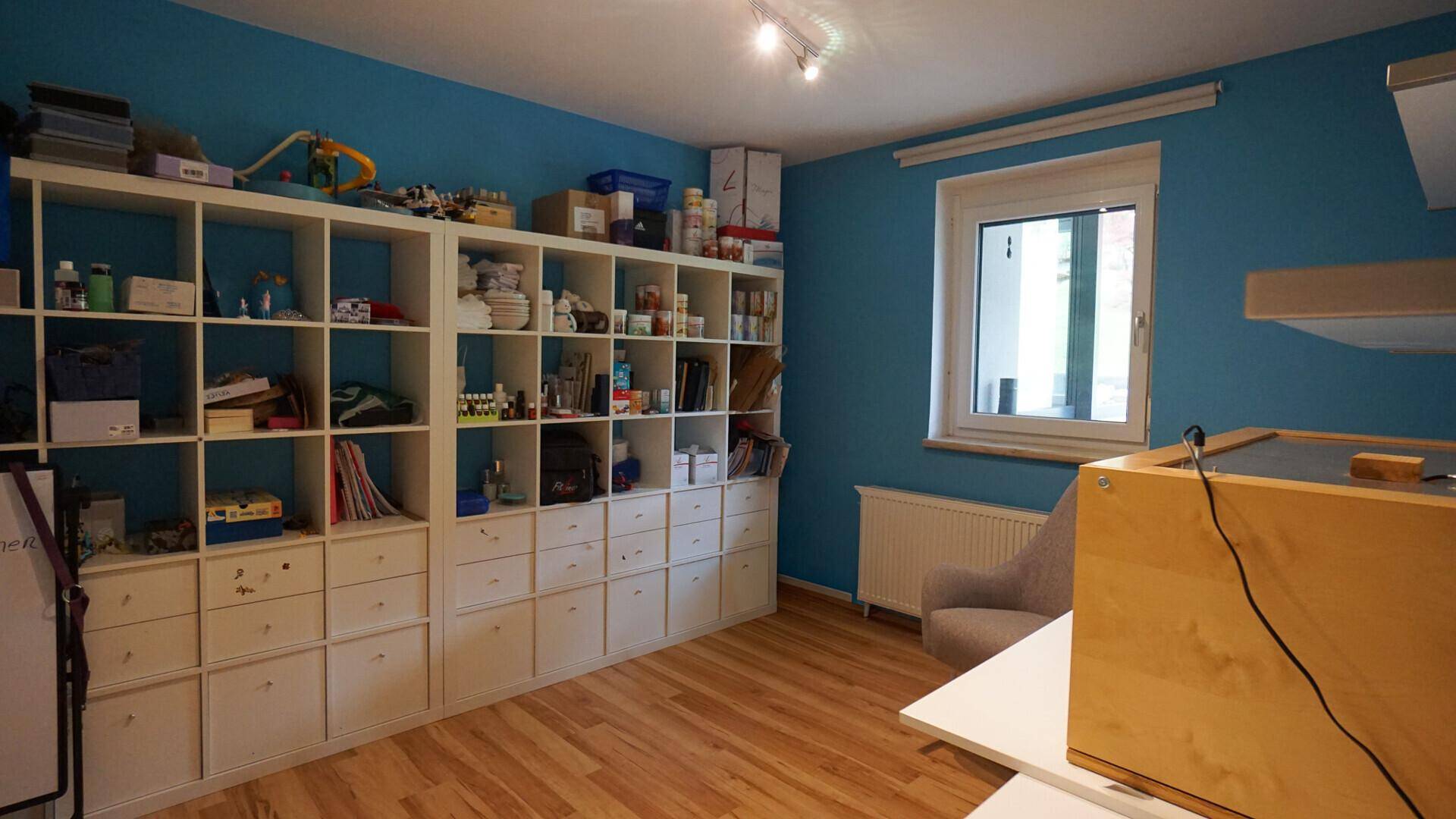 Helles Zimmer mit blauen Wänden, weißen Regalen und Holzfußboden, ideal als Kinderzimmer oder Büro.