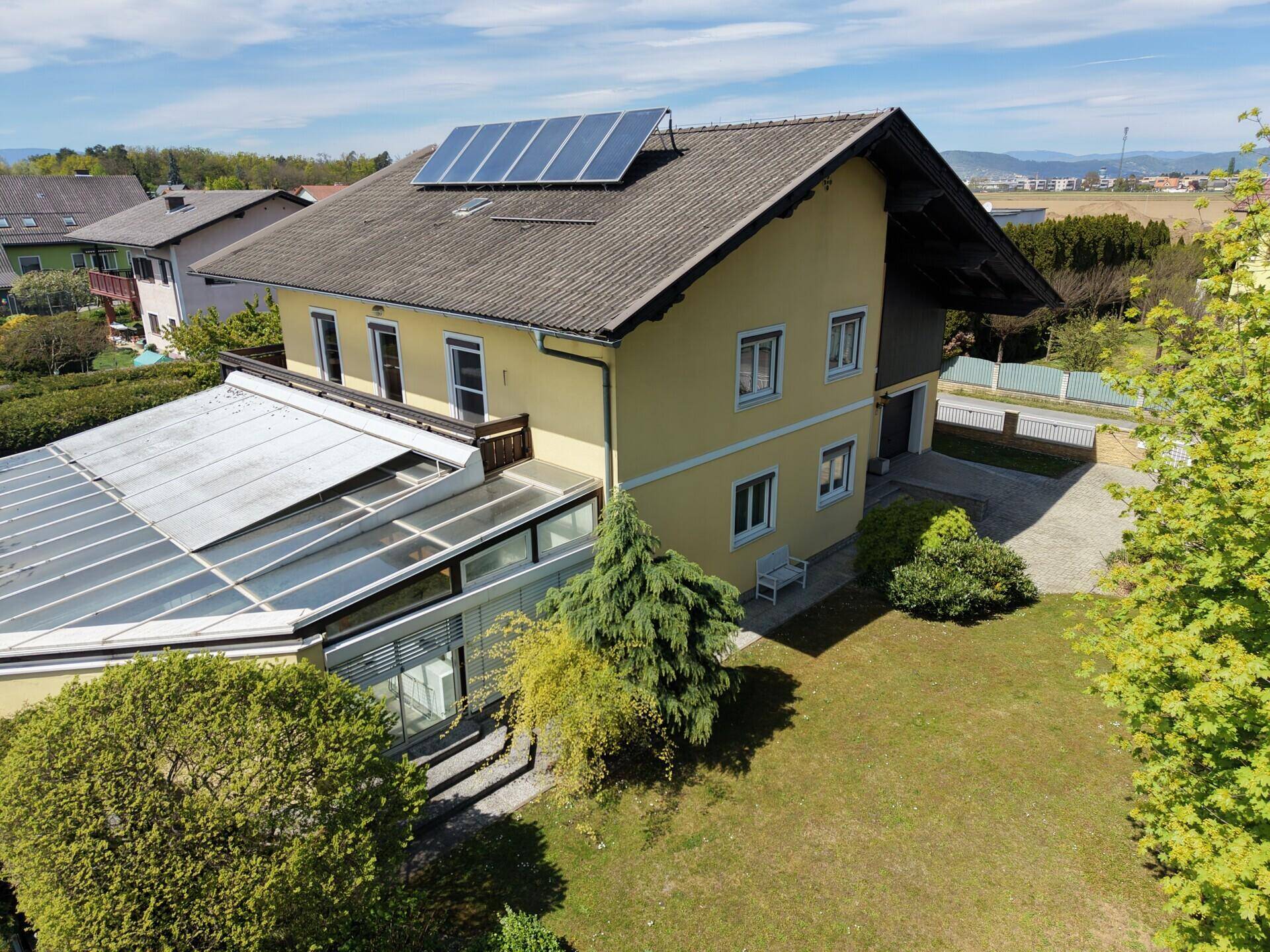 Haus mit gelber Fassade, Solaranlage auf dem Dach und Wintergartenanbau.